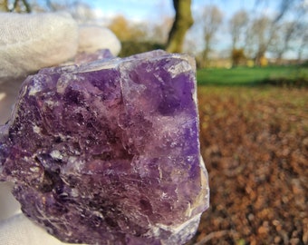May include: A large, purple fluorite crystal with a rough, textured surface. The crystal is translucent and has a slight shimmer.