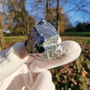Può includere: Un grande cristallo metallico grigio scuro con molteplici sfaccettature. Il cristallo ha una forma geometrica affilata e una superficie riflettente.