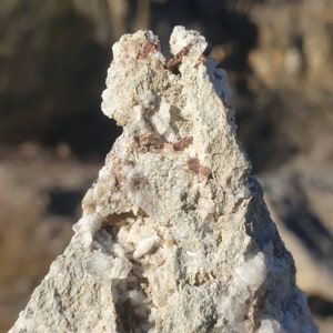 Puede incluir: Primer plano de una formación rocosa con pequeños cristales blancos y depósitos minerales marrones. La roca tiene una superficie rugosa y texturizada.