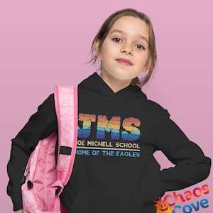 May include: A black hoodie with a rainbow-colored graphic that says "JMS Joe Mitchell School Home of the Eagles". A young person is wearing the hoodie and carrying a pink backpack.