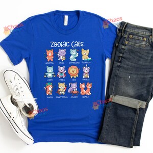 May include: A royal blue t-shirt with a graphic of zodiac cats. The cats are depicted in their respective zodiac signs, with each cat wearing a different color and design. The text "Zodiac Cats" is printed in white above the graphic.