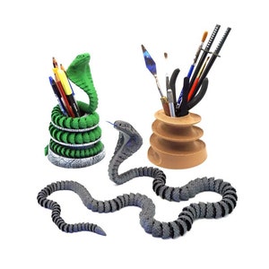 May include: Two 3D printed snake-shaped pencil holders. One is green and holds pens and pencils. The other is gray and holds paintbrushes and tools.