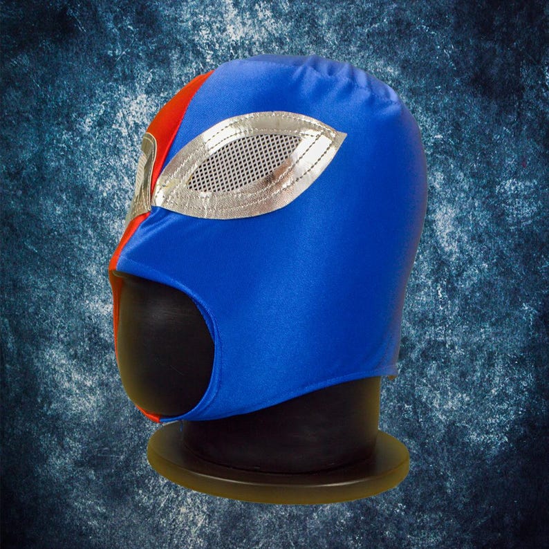 Op de afbeelding: Een blauw en rood worstelmasker met een zilverkleurig oogontwerp. Het masker is gemaakt van een glanzende stof en wordt getoond op een zwarte mannequinhoofd. Het masker heeft een rood gedeelte aan de linkerkant en een blauw gedeelte aan de rechterkant.