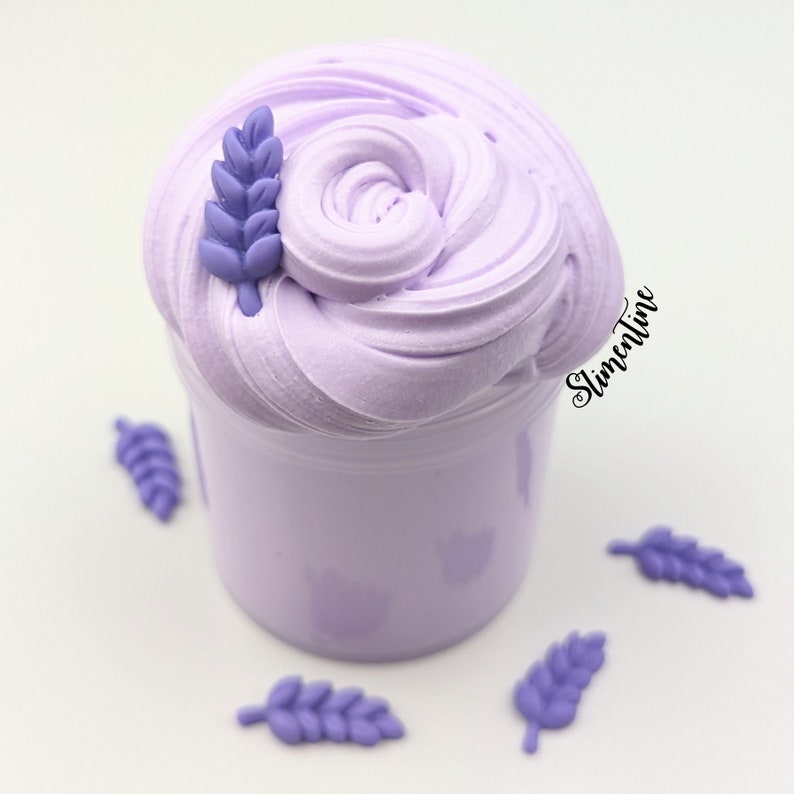 May include: Purple slime in a clear jar with a lavender flower on top. There are several lavender flowers scattered around the jar.