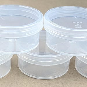May include: Six clear plastic containers with lids. The containers are round and have a capacity of 10 ml.