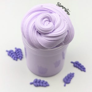 May include: A purple slime in a clear jar with a white background. There are four purple leaf-shaped decorations around the jar.