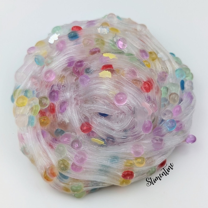 May include: Clear slime with colorful beads and glitter. The slime is in a ball shape and has a light pink hue. The text "SlimeTime" is visible in the bottom right corner of the image.