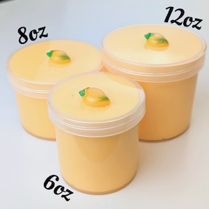 May include: Three clear plastic containers of yellow slime with a small mango-shaped charm on top. The containers are labeled 6oz, 8oz, and 12oz.
