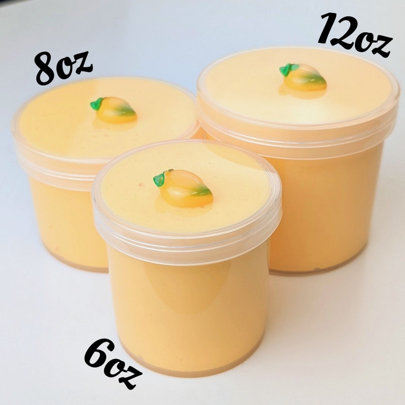 May include: Three clear plastic containers of yellow slime with a small mango-shaped charm on top. The containers are labeled 6oz, 8oz, and 12oz.