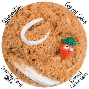 Pode incluir: Um close-up de uma gosma redonda, texturizada, marrom, com redemoinhos de glacê branco. Um pequeno pingente de cenoura laranja com folhas verdes está na gosma. Os textos "Slimentine", "Carrot Cake", "Crunchy Cloud Slime" e "Scented: Carrot Cake" são visíveis.