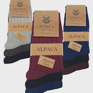 Könnte beinhalten: Drei Paar Alpaka-Wollsocken in Grau, Burgunderrot und Marineblau, jeweils mit einer passenden dunkleren Farbe an Bündchen und Zehen. Jedes Paar ist mit einem braunen Etikett mit der Aufschrift "ALPACA" und "Alpacawolle THERMO" versehen.