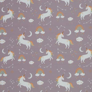 Puede incluir: Un patrón repetitivo con unicornios blancos con cuernos dorados y crines y colas coloridas. El diseño también incluye arcoíris, nubes, lunas crecientes y constelaciones sobre un fondo morado apagado.