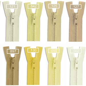 May include: A collection of eleven nylon coil zippers arranged in two rows, featuring various shades of beige, cream, yellow, and tan. Each zipper includes a matching slider and a white rectangular label with a specific color code number.