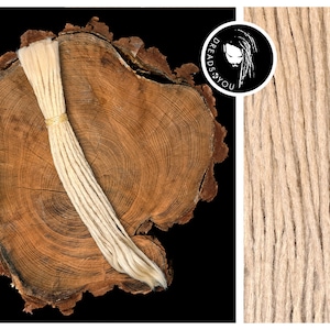 Könnte beinhalten: Ein Bündel hellblonder synthetischer Dreadlocks, mit einem goldenen Band zusammengebunden, auf einer Holzoberfläche. Die Dreadlocks sind aus Kanekalon-Haar gefertigt und etwa 50 cm lang.