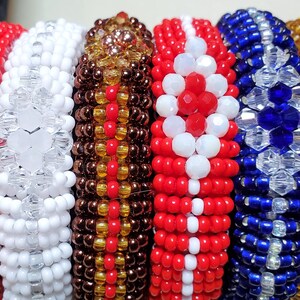 May include: A collection of beaded bracelets in various colors, including black, red, white, brown, blue, and yellow. The bracelets are made with small, round beads and are arranged side by side, showcasing their intricate designs and vibrant hues.