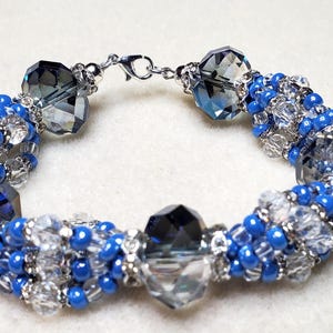May include: A blue and silver beaded bracelet with crystal accents. The bracelet is made with small blue beads, clear beads, and larger crystal beads.