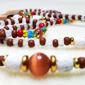 May include: A collection of beaded necklaces. The necklaces feature brown, clear, and white beads, accented with gold-colored metal and a large, orange-brown bead. The beads are strung together to create a layered effect, suitable for jewelry.