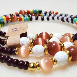 May include: A multi-strand beaded necklace with brown, white, and orange beads. The necklace features a variety of bead sizes and shapes, including small round beads, larger round beads, and small white beads with a textured surface.