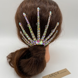 May include: A crystal hair comb with a fan-shaped design. The comb is made of clear crystals with iridescent rainbow colors. The comb is attached to a brown hair mannequin.