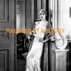 Puede incluir: Una mujer con un camisón blanco de satén con ribetes de encaje se encuentra de pie en una puerta. Lleva una bata con ribetes de piel y tiene el pelo peinado con un bob corto y ondulado. El texto "HAUNTED BY HISTORY" está superpuesto sobre la imagen.