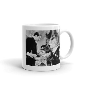 May include: White ceramic mug featuring a black and white image of a vintage film scene. The image shows a man and a woman at a table, with ornate details. The mug has a curved handle and a glossy finish.
