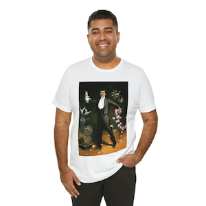 Peut inclure: Un t-shirt blanc avec une illustration vintage d'un magicien effectuant un tour de magie. Le magicien porte un smoking noir et est entouré de colombes, de fleurs et d'une boîte.