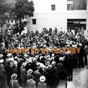 May include: A black and white photograph of a large group of people gathered in a courtyard. The people are wearing hats and suits. The photo is taken from a high angle, looking down on the group. The text "HAUNTED BY HISTORY" is superimposed over the image.