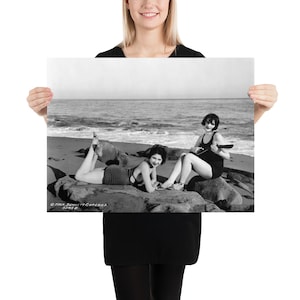 Könnte beinhalten: Zwei Frauen in Badeanzügen am Strand. Eine Frau liegt auf einem Felsen, während die andere auf einem Felsen sitzt und Ukulele spielt.