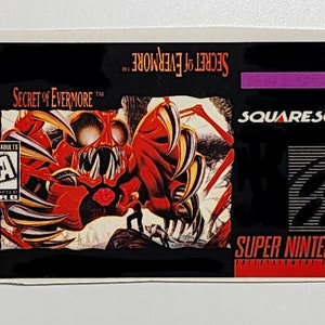 May include: A black Super Nintendo game cartridge with a red and black label. The label features a monster with sharp claws and teeth. The game title is "Secret of Evermore" and the publisher is "Squaresoft".