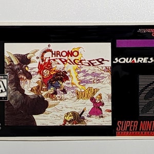 May include: A black and white Super Nintendo game cartridge label for Chrono Trigger, featuring a purple and white logo for SquareSoft. The label also includes a black and white image of a character from the game.