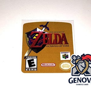 May include: A yellow, gold, and blue Nintendo 64 video game cartridge label for The Legend of Zelda: Ocarina of Time. The label features a stylized image of Link's sword and shield, along with the game's title and rating.