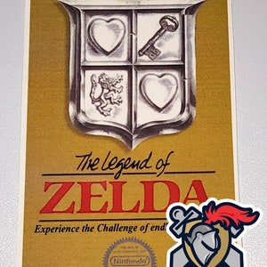 May include: A gold Nintendo Entertainment System game cartridge for The Legend of Zelda. The front of the cartridge features a gold shield with a key, a heart, and a lion. The text "The Legend of Zelda" is printed in red letters below the shield. The text "Experience the Challenge of end" is printed below the title. The text "Made in Japan" is printed in the bottom left corner. The Nintendo seal is printed in the bottom right corner.