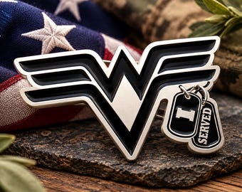 May include: A metallic pin featuring a stylized black and silver W-shaped emblem. Attached to the right side are two small, rectangular dog tag charms. One charm displays the letter I, and the other features the text SERVED in white lettering.