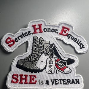 May include: Embroidered patch with the words "Service, Honor, Equality" and "SHE is a VETERAN" in red and white. The patch features images of combat boots, dog tags, high heels, and a red and white sneaker.