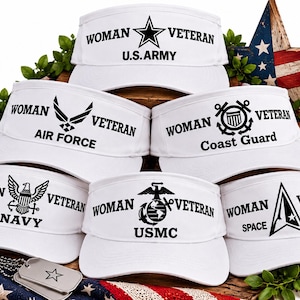 May include: A collection of six white sun visors, each featuring black text and military branch emblems. The visors are labeled for Woman Veteran with specific branch designations including U.S. Army, Air Force, Coast Guard, Navy, USMC, and Space Force.