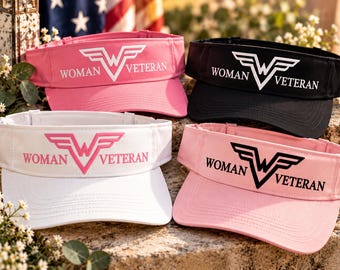 May include: Four sun visors in pink, black, white, and light pink. Each visor features a winged W logo and the text WOMAN VETERAN printed on the front band. The visors have an adjustable strap at the back and a curved brim for sun protection.
