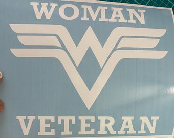 May include: A light blue vinyl decal featuring the white text WOMAN at the top and VETERAN at the bottom, with a large white stylized W emblem in the center. The design is printed on a rectangular light blue backing sheet.
