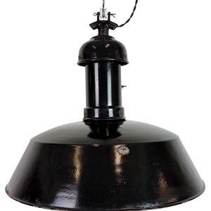 Könnte beinhalten: Eine schwarze Industrie-Pendelleuchte mit breitem, konischem Schirm. Die Leuchte hat einen zylindrischen Körper und eine Metallaufhängung. Der Schirm hat eine glänzende Oberfläche und weist Gebrauchsspuren auf. Das Licht wird von einem Draht abgehängt.