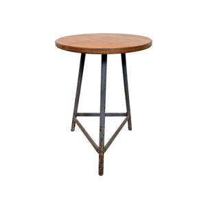 Op de afbeelding: Een kleine, ronde bijzettafel met een houten blad en een metalen onderstel. Het tafelblad is lichtbruin en het onderstel is gemaakt van donkergrijs metaal. De tafel is ongeveer 61 cm hoog en 51 cm in diameter.