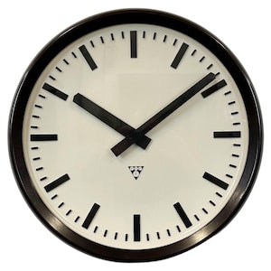May include: A round wall clock with a cream-coloured face and a dark brown frame. The clock features black hour markers and hands, with a small logo at the bottom. The clock's diameter is approximately 30 cm.