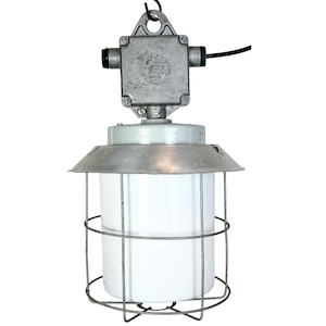 Op de afbeelding: Een zilveren hanglamp met een kooi en een witte glazen kap en een metalen haak aan de bovenkant. De lamp heeft een zilveren elektrische doos met een zwarte draad.