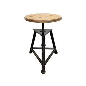 Op de afbeelding: Een in hoogte verstelbare kruk met een ronde houten zitting en een zwart metalen onderstel. De zitting heeft een diameter van ongeveer 35 cm. De basis heeft een driepootontwerp.