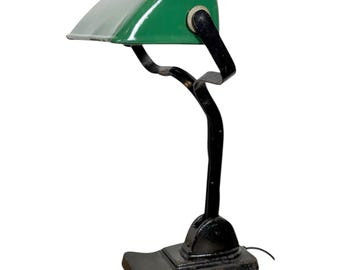 Könnte beinhalten: Vintage Schreibtischlampe in Grün und Schwarz. Die Lampe hat einen geschwungenen grünen Schirm und einen schwarzen, geschwungenen Arm und Sockel. Der Sockel ist rechteckig. Die Lampe ist für einen Schreibtisch oder Tisch konzipiert und hat ein Netzkabel. Ca. 30 cm hoch.