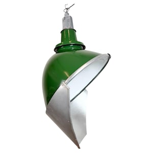 Puede incluir: Lámpara colgante industrial verde con interior blanco y pantalla de metal plateado. La lámpara tiene una parte superior redondeada y un mecanismo de suspensión metálico. La pantalla está en ángulo y la luz está suspendida de un cable.