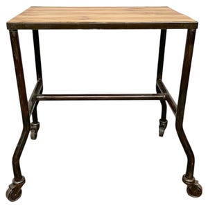 Könnte beinhalten: Industrieller Tisch mit heller Holzplatte und dunklem Metallrahmen. Der Rahmen hat gebogene Beine und Rollen. Der Tisch ist ca. 76 cm lang. Ideal für ein Wohnzimmer oder eine Werkstatt.
