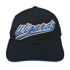 Puede incluir: Una gorra de béisbol negra con la palabra Wizards bordada en letra cursiva azul con un contorno dorado en los paneles frontales. La gorra tiene una corona estructurada, una visera curva con borde azul y ojales de ventilación superiores.