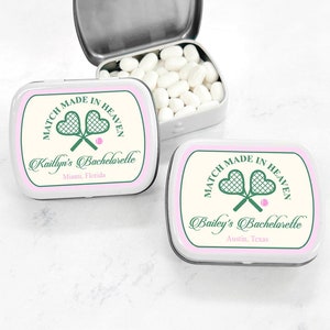 May include: Two white metal mint tins with pink and green labels. The labels have a tennis racket design and the text "Match Made in Heaven". One tin says "Kaillyn's Bachelorette, Miami, Florida" and the other says "Bailey's Bachelorette, Austin, Texas".
