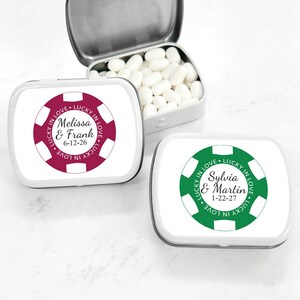 May include: Two small white metal tins with personalized labels. The labels are round and feature a red and green casino chip design with the text "Lucky in Love" and the names of the couples and their wedding dates.