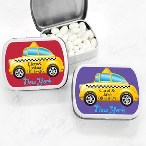 May include: Two yellow and black New York City taxi cab themed mint tins. The tin on the left has a red background and says "Elena & Joshua 10-15-26 New York". The tin on the right has a purple background and says "Carol & Jake 08-20-27 New York".