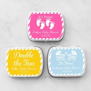 May include: Three white mint tins with colorful labels. The pink tin has a pair of footprints and the text "It's Twins! Evelyn's Baby Shower 6.19.24". The yellow tin has the text "Double the Fun Kelly's Baby Shower 7.21.25". The blue tin has two baby carriages and the text "It's Twins! Brittany's Baby Shower 10.28.26".